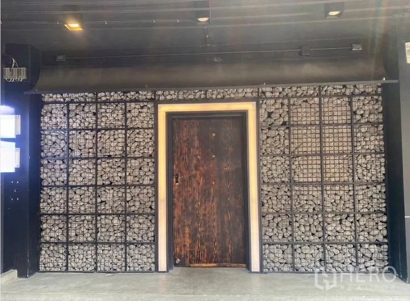 Shophouse for rent - Shophouse facade with gabion stone wall and a rustic wooden door under dark awning lighting.