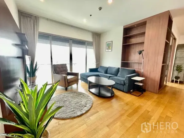 公寓 出租在Watthana, Bangkok - 明亮客厅，布艺沙发、内置书架与落地玻璃门通往阳台，城市景观。