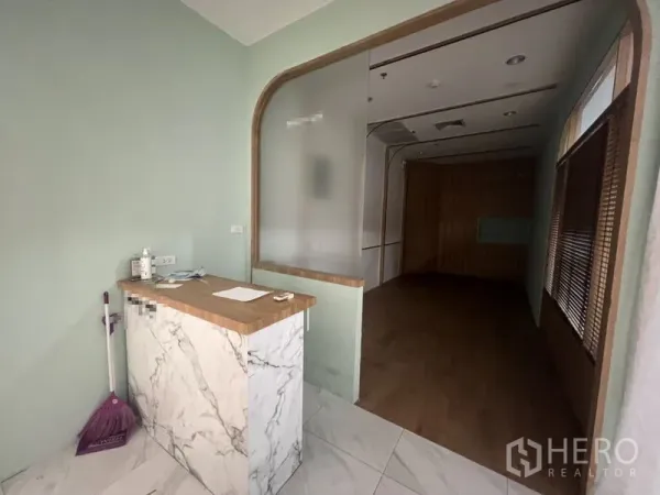 Retail Space for rent in Watthana, Bangkok - Reception corner with marble-look counter, mint walls, frosted glass, and a wood-floored sales area beyond.