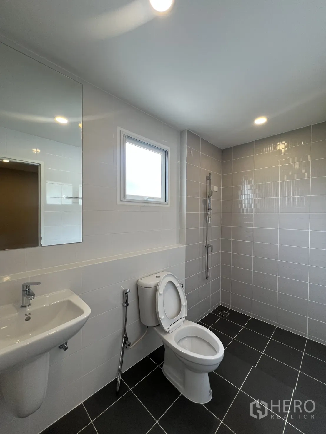 独栋房屋 for rent in Lat Krabang, Bangkok - 现代卫浴设洗手盆、坐便、手持花洒与灰色墙砖及小窗。