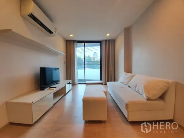 Condominium for rent in Watthana, Bangkok - Bright living room of a 2-bedroom Watthana condo with sofa, TV unit, wood floors and sliding door to a balcony.