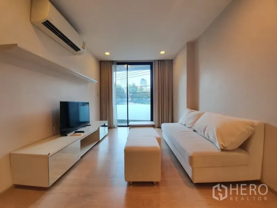 公寓 出租在Watthana, Bangkok - 瓦他那区两卧公寓明亮客厅，木地板，沙发与电视柜，推拉门连接阳台。