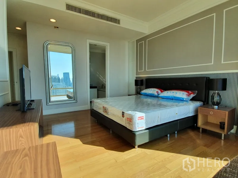 公寓 出租在Watthana, Bangkok - 宽敞主卧，墙面线条装饰，电视柜，通往套内卫浴并可观城市景观。