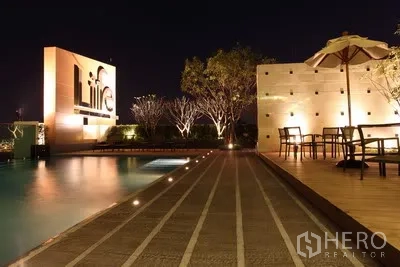 公寓 出租在Watthana, Bangkok - 夜间公寓泳池与露台座位，发光项目标识与氛围灯光