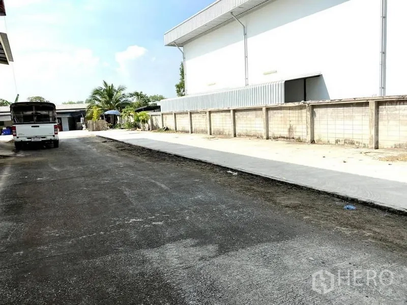 Warehouse for rent in Lam Luk Ka, Pathum Thani - Wide driveway for trucks alongside the warehouse and perimeter wall.