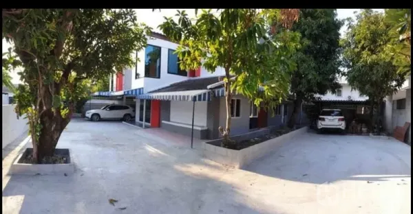 Detached House for rent in Lat Phrao, Bangkok - Front exterior of a two‑storey detached house in Lat Phrao with wide concrete driveway, mature trees and dual carports.