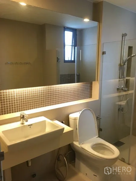 Detached House for rent or sale in Bang Kapi, Bangkok - Bathroom with illuminated mirror, vanity sink, toilet and glass shower enclosure.