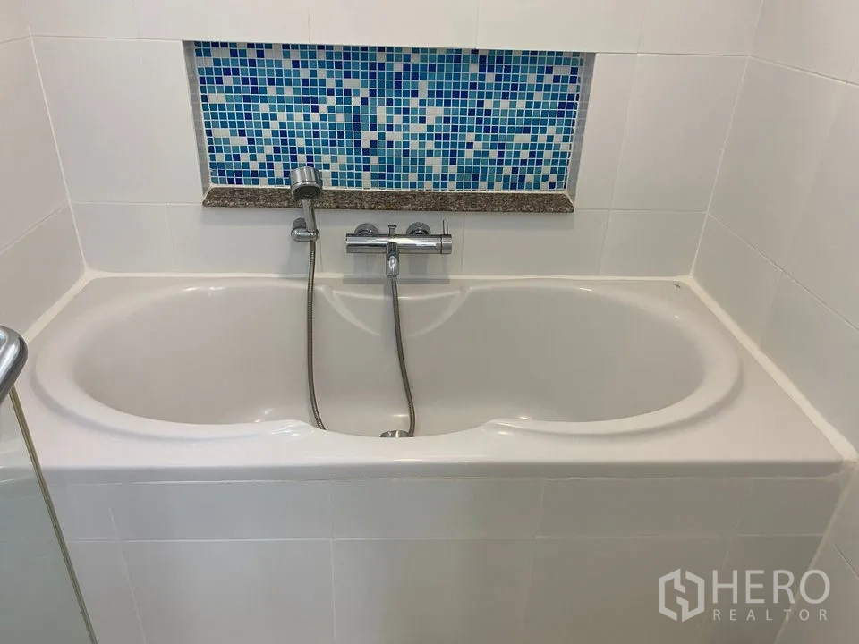 Condominium for rent or sale in Phra Khanong, Bangkok - White bathtub with handheld shower and blue mosaic niche.