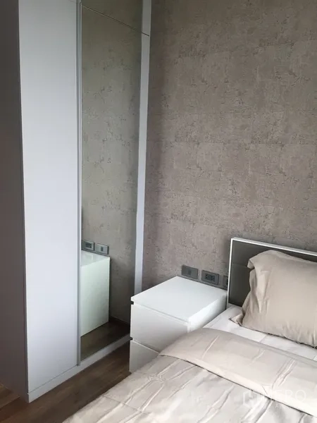 Condominium for rent in Watthana, Bangkok - Bedroom corner with a white mirrored wardrobe and bedside table against a textured wall.