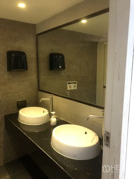 Office Space for rent - Modern restroom featuring twin vessel sinks, a large mirror, and gray wall tiles.