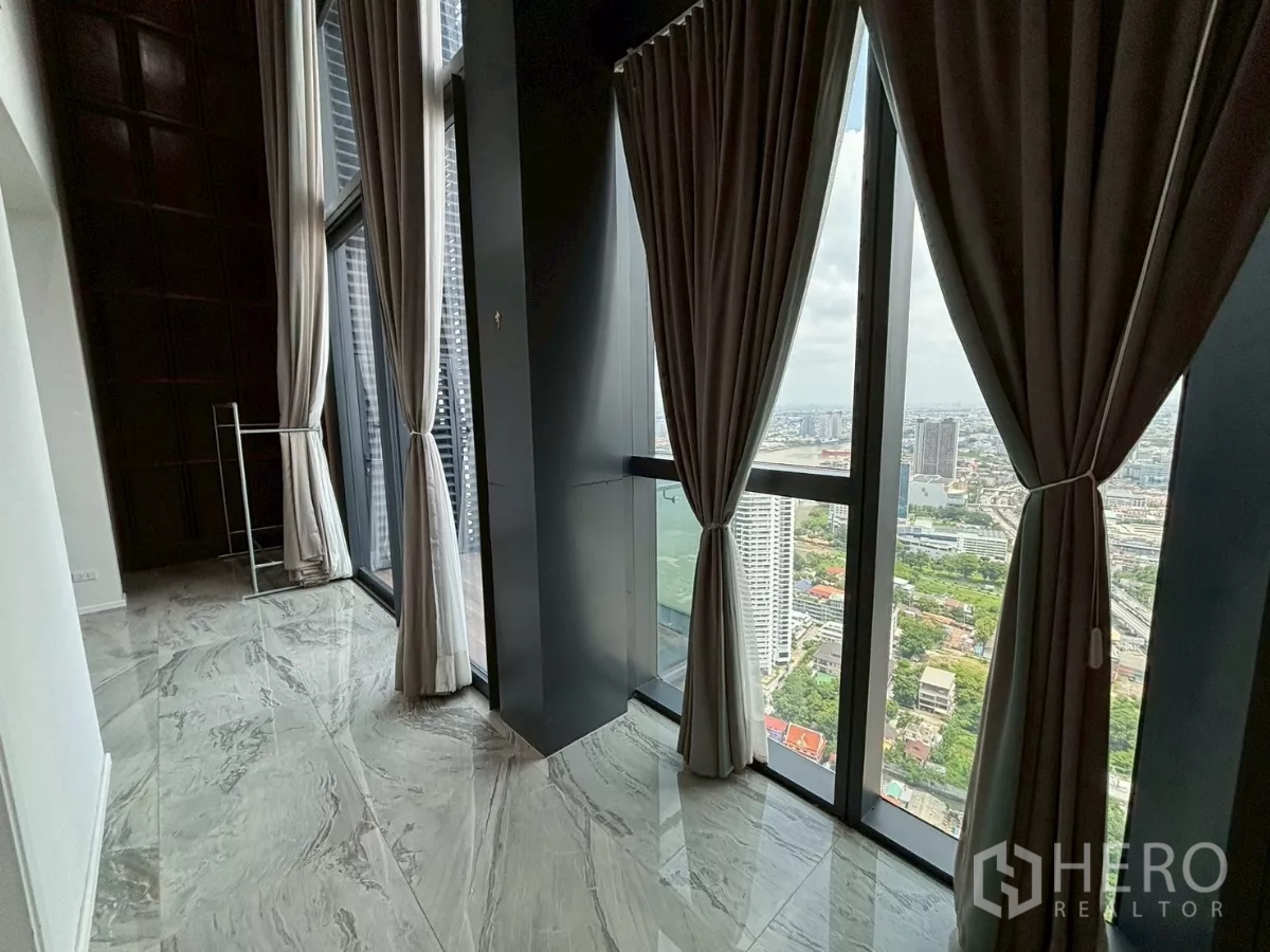 Condominium for sale in Bang Kho Laem, Bangkok - Tall glass windows with curtains framing skyline and river glimpse from a high floor.