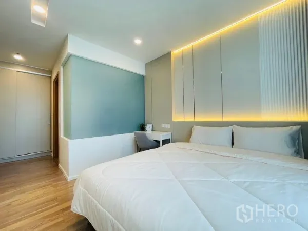Condominium for rent in Khlong Toei, Bangkok - Serene master bedroom with wood floors, soft LED wall feature, built-in wardrobe and a compact work desk.