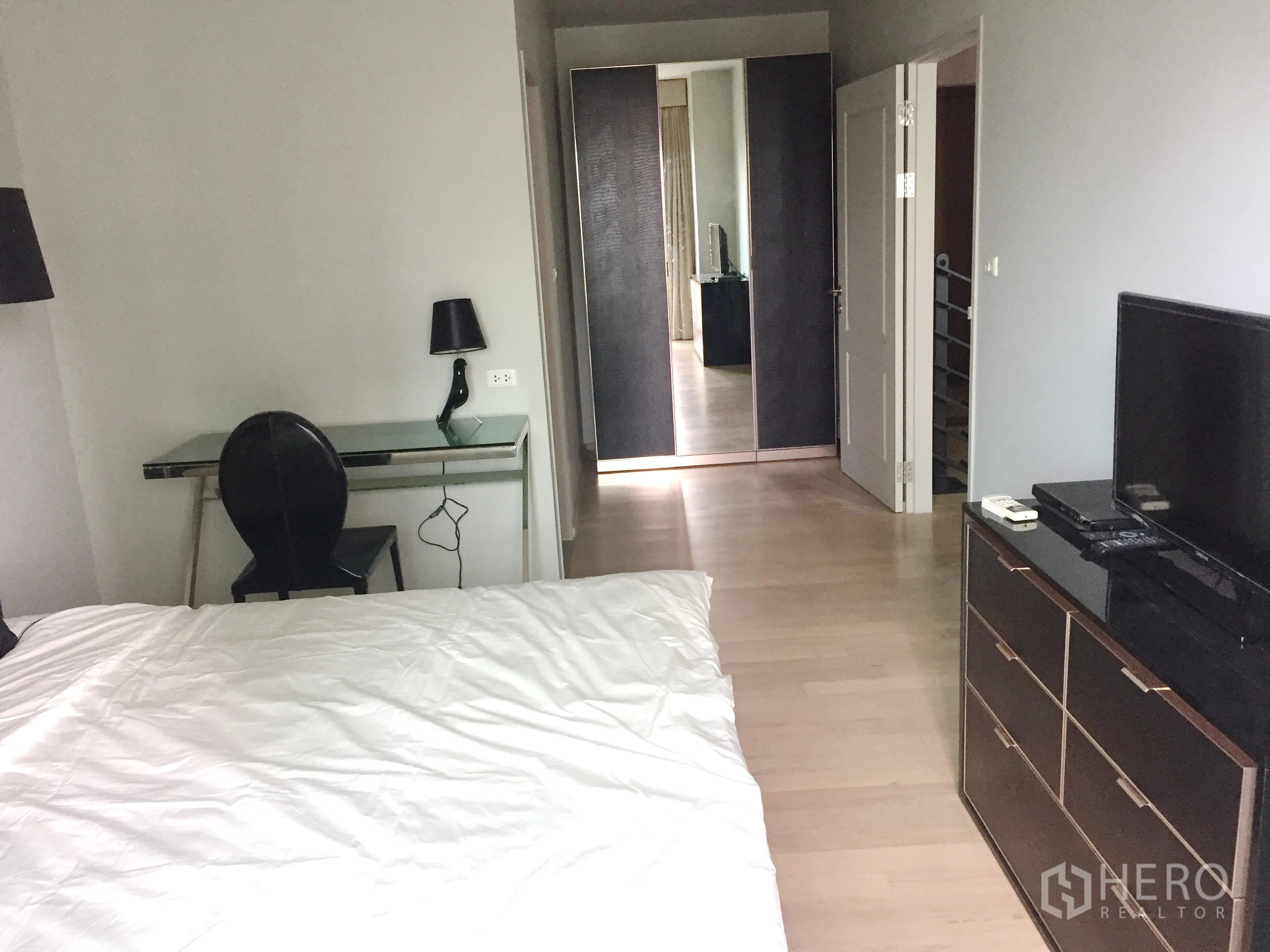 Condominium for rent in Bangkok - Bedroom angle showing wardrobe with mirrors, work desk, TV cabinet and light wood flooring.