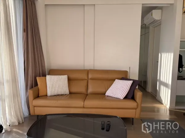 公寓 出售在Watthana, Bangkok - 客厅内棕色真皮沙发，推拉隔断与通往卧室的走廊。