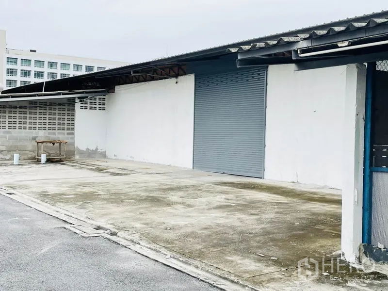 Factory for rent in Bang Pakong, Chachoengsao - Single warehouse bay with closed roller door and ample loading space beside a low block wall.