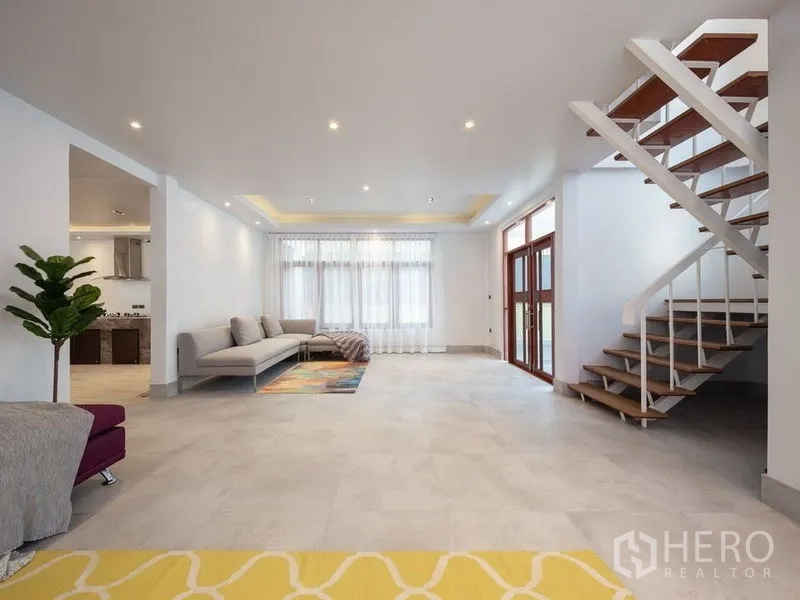 Detached House for sale in Chatuchak, Bangkok - Large living room with open staircase, recessed ceiling lights and tiled floors.