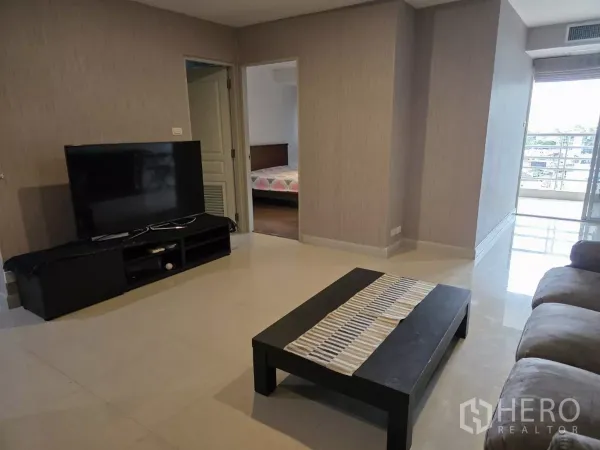 公寓 出租在Khlong Toei, Bangkok - 宽敞客厅设电视柜与茶几，可通往卧室和阳台。