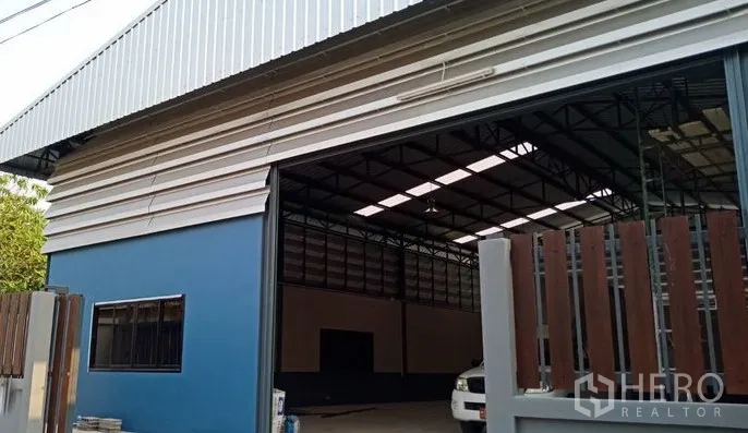货栈 出售在Pathum Thani - 卷帘门部分开启，可见钢桁架屋顶与蓝灰色仓库装卸区。