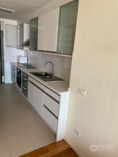 Condominium for rent in Khlong Toei, Bangkok - Galley kitchen with white cabinetry, sink, cooktop, and oven.