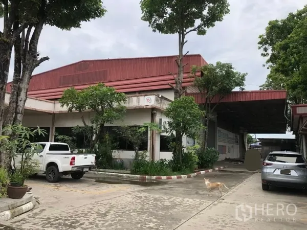 Factory for sale in Lam Luk Ka, Pathum Thani - Industrial factory exterior with red roof, landscaped frontage and wide parking driveway.