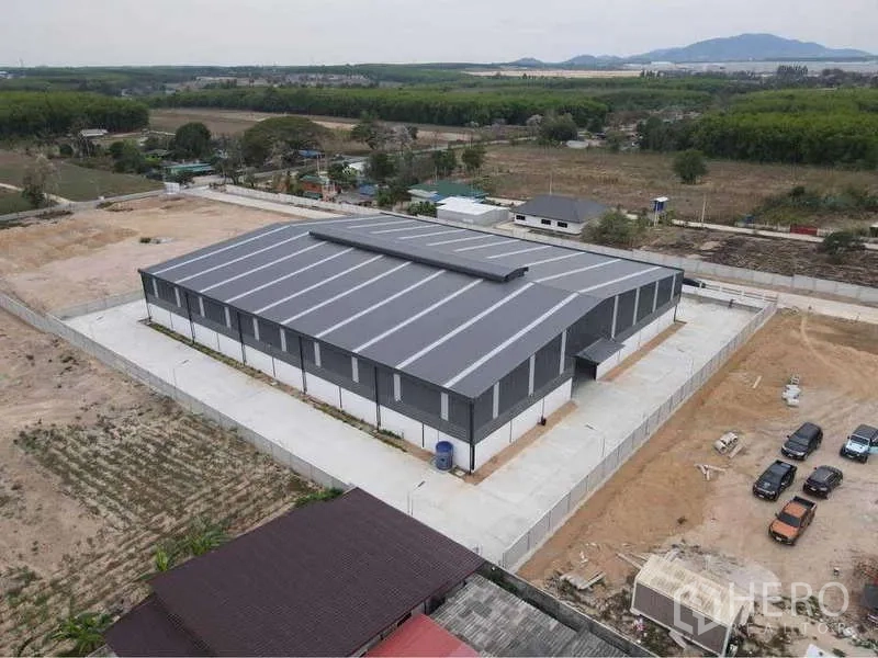 货栈 出租或出售在Nikhom Phatthana, Rayong - 后侧航拍视角，整栋仓库屋顶、混凝土车道及周边绿地一览。