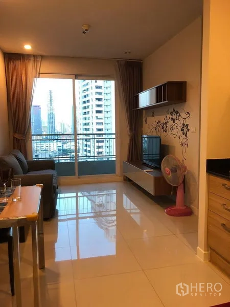 คอนโด ขายในRatchathewi, Bangkok - ห้องนั่งเล่นสว่าง มีประตูกระจกเปิดสู่ระเบียง มองเห็นวิวตึกเมือง พร้อมชั้นลอยและชั้นวางทีวี