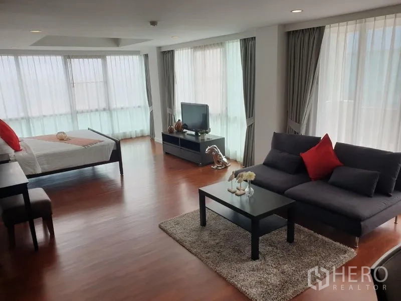 公寓 出租在Bang Rak, Bangkok - 转角套房，多个落地窗、灰色沙发、电视柜与温润木地板。