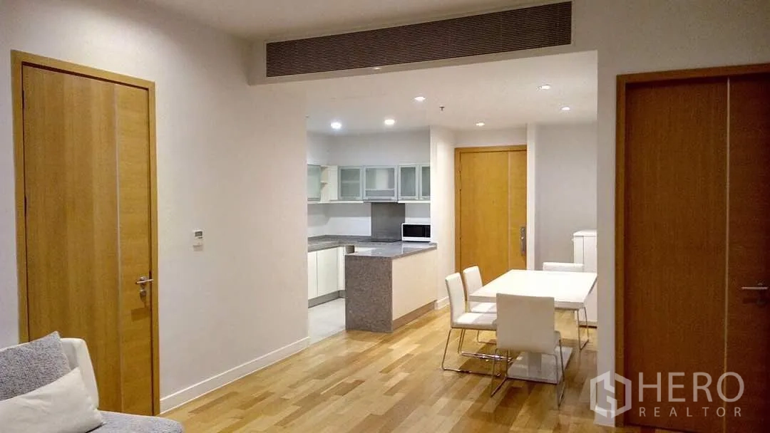 Condominium for rent or sale in Khlong Toei, Bangkok - Spacious layout with light wood floors, dining set, and kitchen with glass-front cabinets in a contemporary condo.