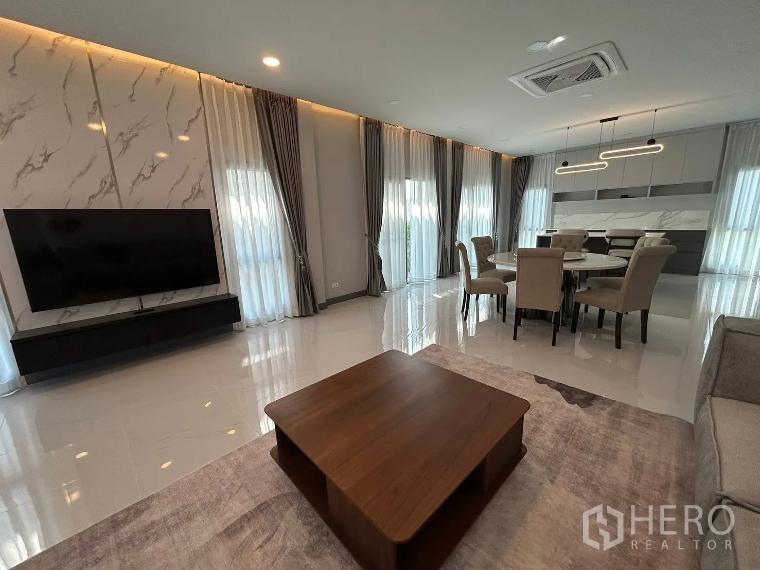 Detached House for rent in Bang Phli, Samut Prakan - Bright living and dining room with TV feature wall, floor-to-ceiling windows, and glossy tile floors.