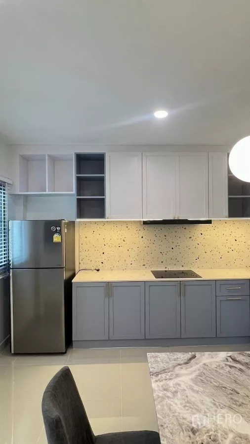 Townhouse for rent in Bang Phli, Samut Prakan - L-shaped kitchen with two-tone cabinets, stone-look backsplash and stainless fridge.