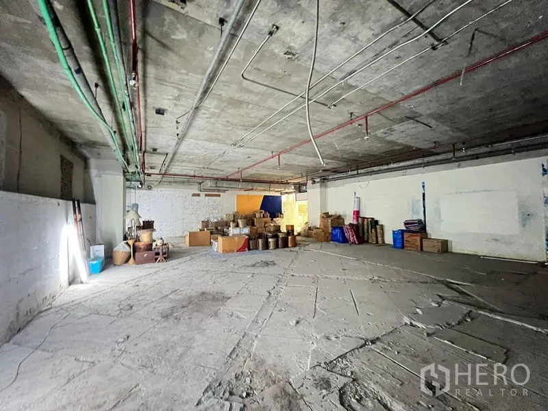 Retail Space for rent - Wide-angle view of a large concrete retail floor with visible service pipes and storage boxes.
