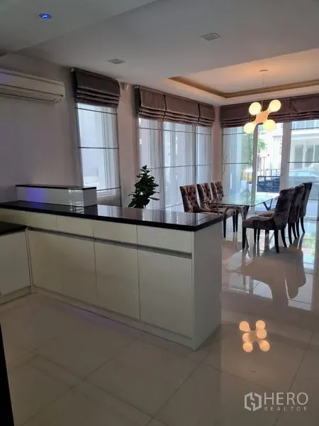Detached House for sale in Chatuchak, Bangkok - Open-plan kitchen with a large island and dining area featuring modern pendant lighting and tall windows.