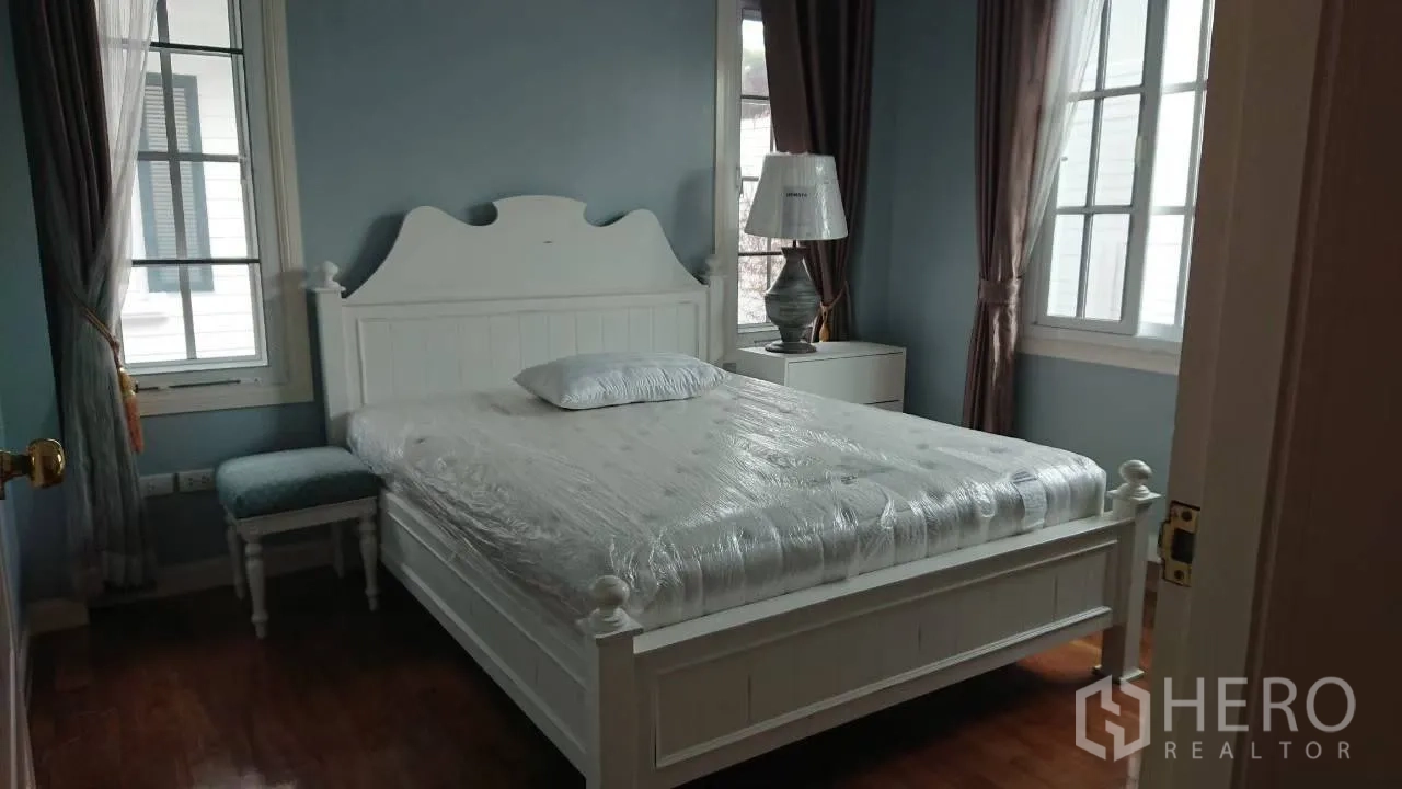 Detached House for rent in Mueang Samut Prakan, Samut Prakan - Cozy bedroom with white bedframe, blue walls and large curtained windows.
