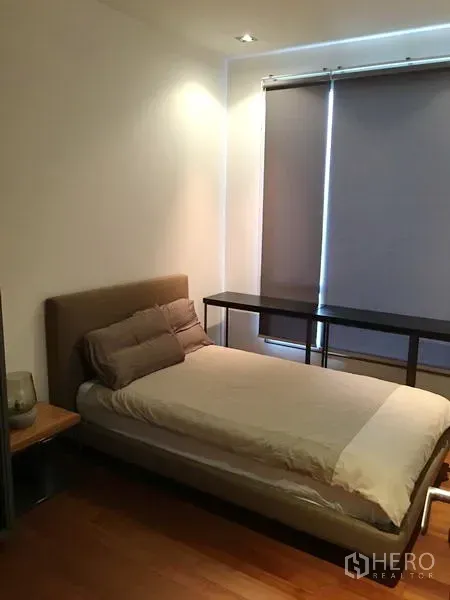 Condominium for rent or sale in Khlong Toei, Bangkok - Bedroom with upholstered bed, blackout blinds and long desk over warm wood floors.