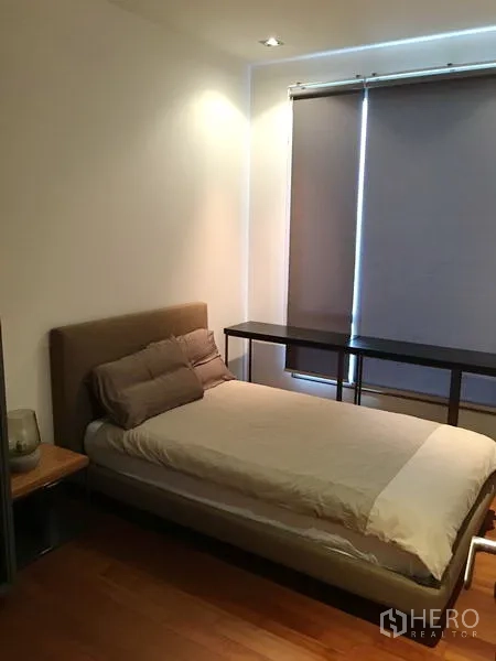 Condominium for rent or sale in Khlong Toei, Bangkok - Bedroom with upholstered bed, blackout blinds and long desk over warm wood floors.