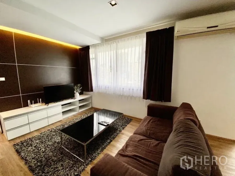 Condominium for rent in Khlong Toei, Bangkok - Living room angle showing TV console, brown sofa, black coffee table and area rug.