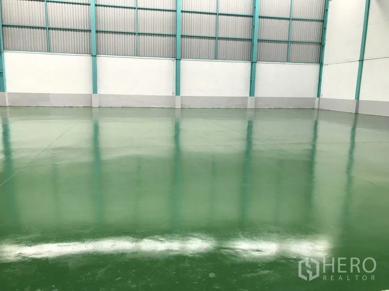 Factory for rent in Samut Prakan - Wide clear‑span warehouse interior showing green epoxy flooring and high ceiling.