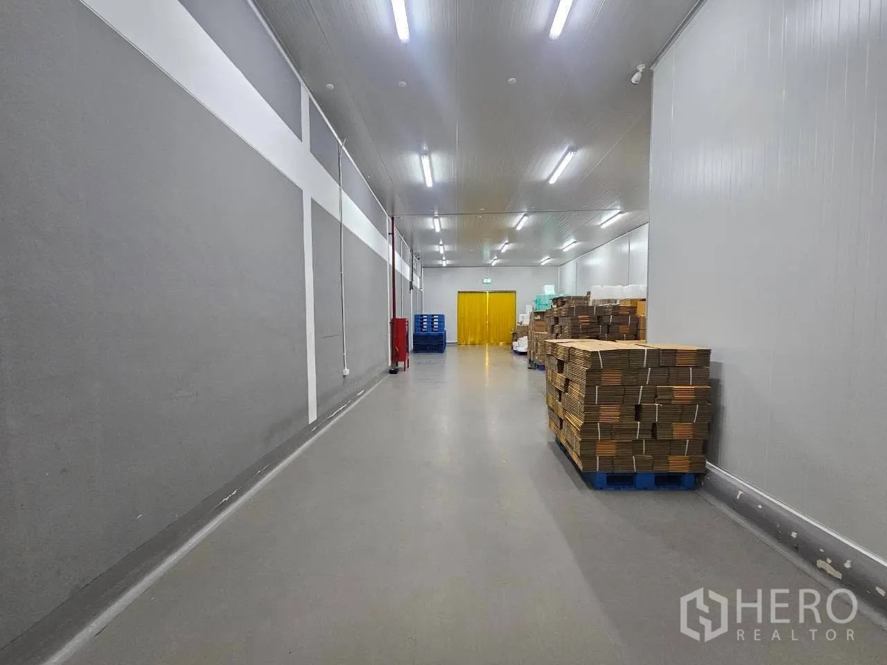 โรงงาน for rent in Mueang Samut Sakhon, Samut Sakhon - โถงเก็บสินค้าภายในยาว ผนังสีเทา พาเลท และไฟดาวน์ไลท์สว่าง