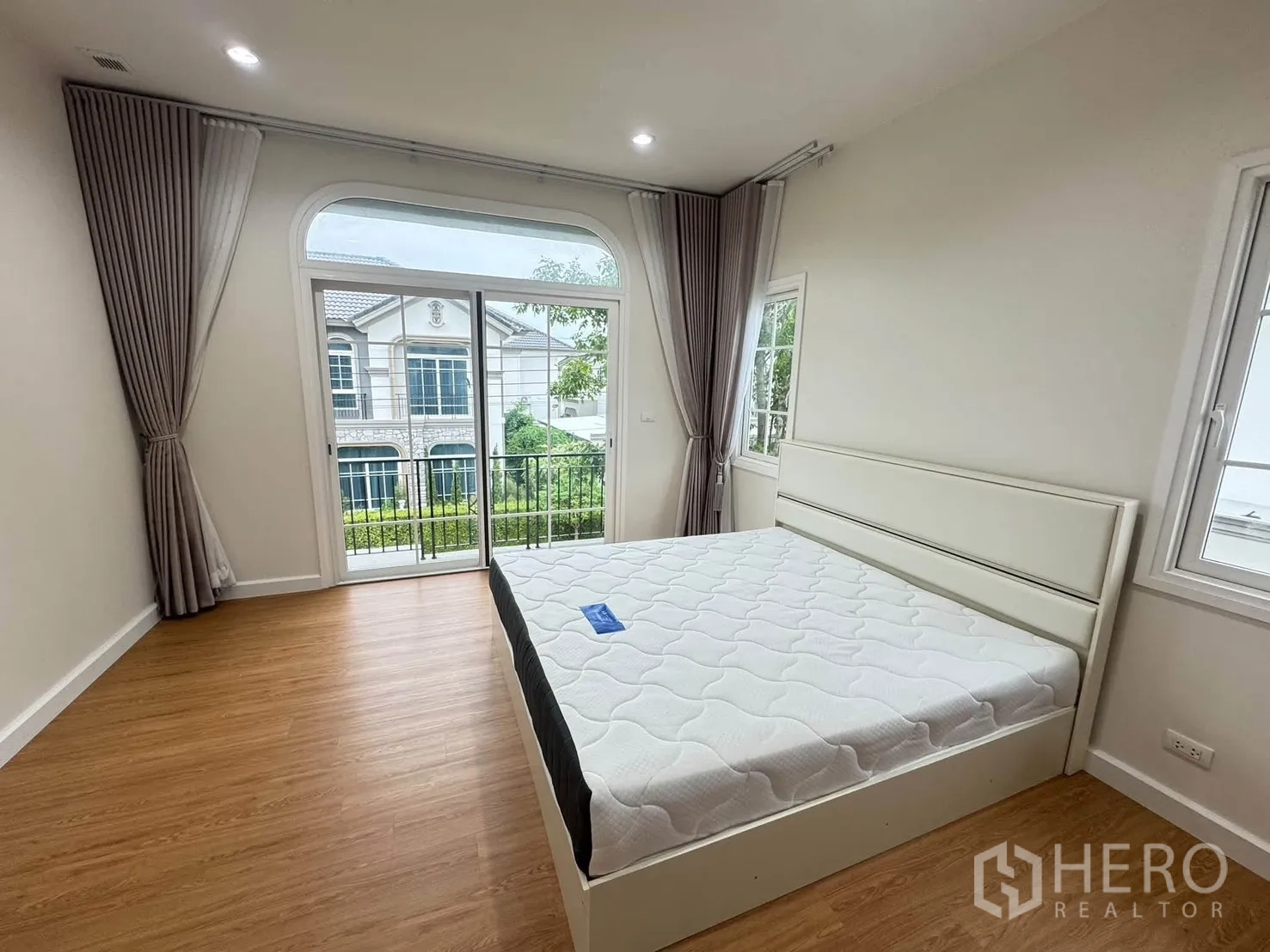 Detached House for rent or sale in Bang Phli, Samut Prakan - Spacious bedroom with wood floors, balcony doors and full-length curtains.