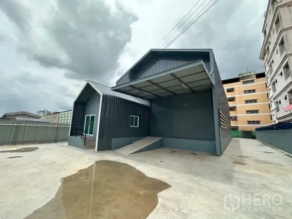 Factory for rent in Khlong Luang, Pathum Thani - Wide concrete yard with covered loading bay, roller shutter, and adjoining office wing.