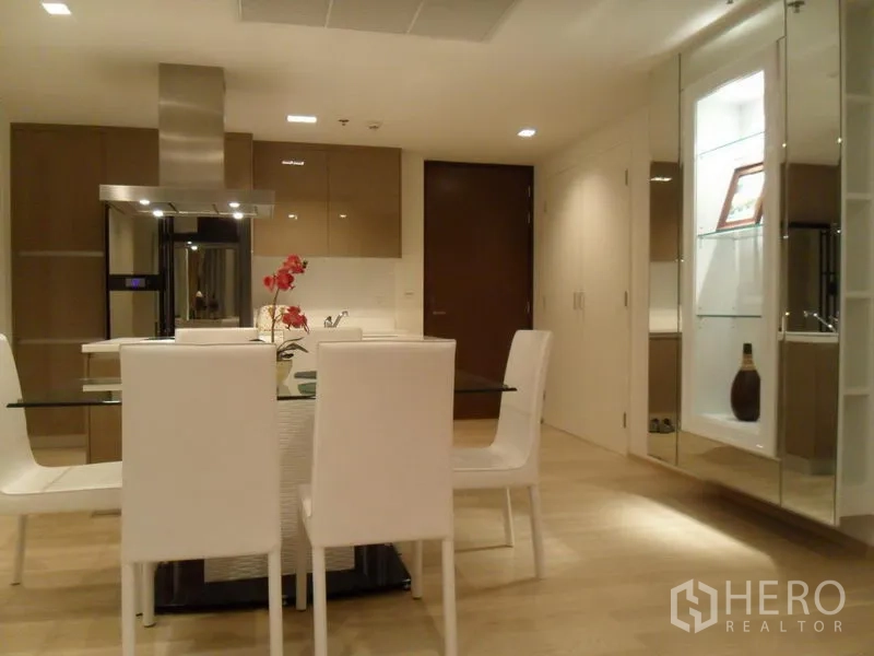 Condominium for rent in Khlong Toei, Bangkok - Dining area with glass table and four white chairs beside a modern open kitchen.