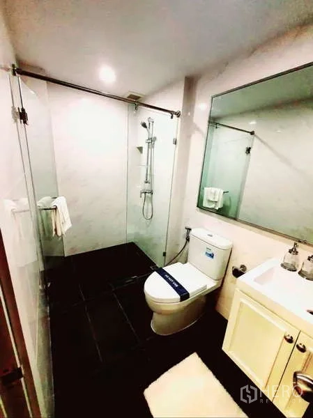 Condominium for sale in Bang Rak, Bangkok - Contemporary bathroom with glass-enclosed shower, toilet, large mirror and vanity.