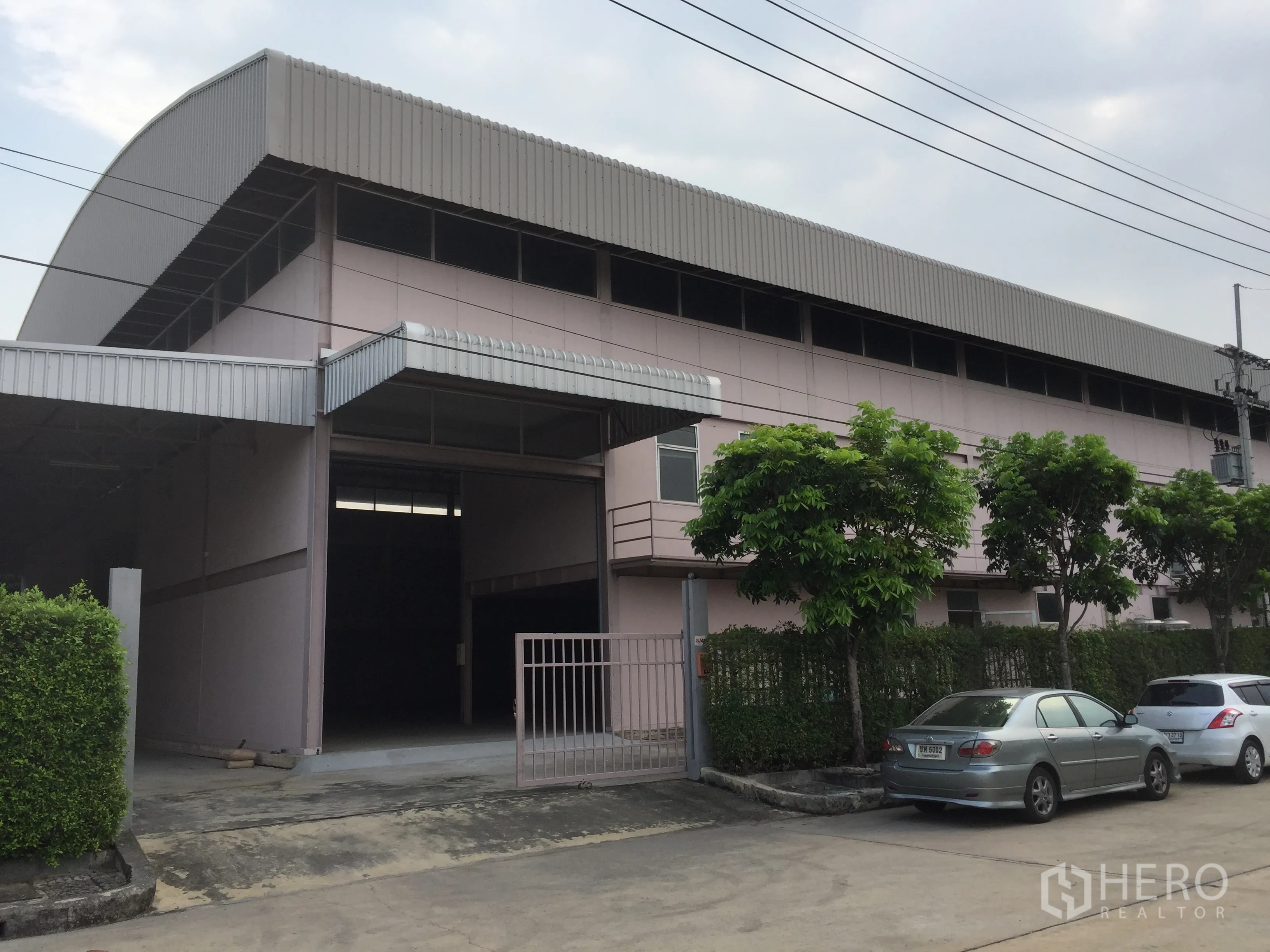 Factory for rent in Lam Luk Ka, Pathum Thani - Large factory exterior in Lam Luk Ka with roller shutter, gated entrance, trees and parking bays.