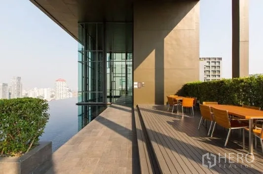 Condominium for rent in Khlong Toei, Bangkok - Sky deck with tables beside a glass facade and greenery overlooking the city.