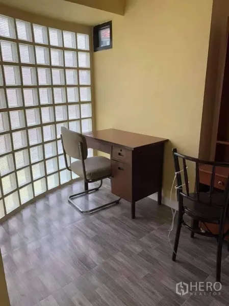 Townhouse for rent in Phra Khanong, Bangkok - Bright study corner with desk beside a glass-block wall and grey wood-look floor tiles.