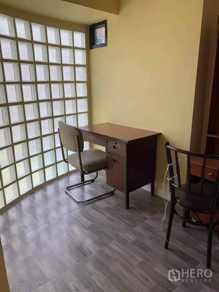 Townhouse for rent in Phra Khanong, Bangkok - Bright study corner with desk beside a glass-block wall and grey wood-look floor tiles.