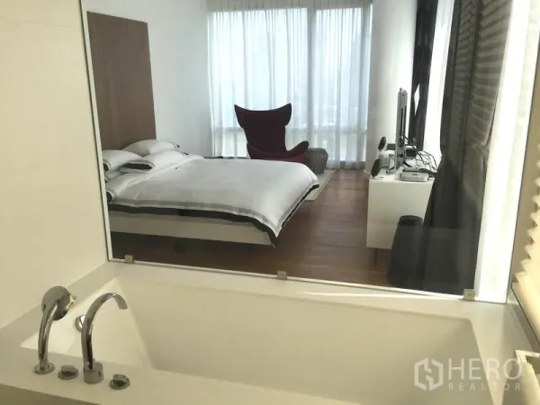 Condominium for rent or sale in Pathum Wan, Bangkok - Soaking bathtub looking through an interior window into the bedroom with sheer curtains