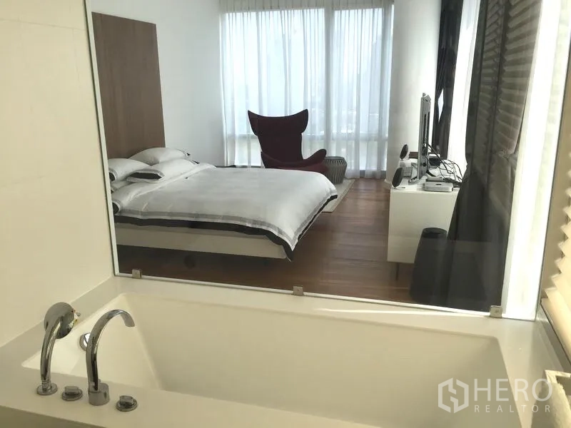 Condominium for rent or sale in Pathum Wan, Bangkok - Soaking bathtub looking through an interior window into the bedroom with sheer curtains