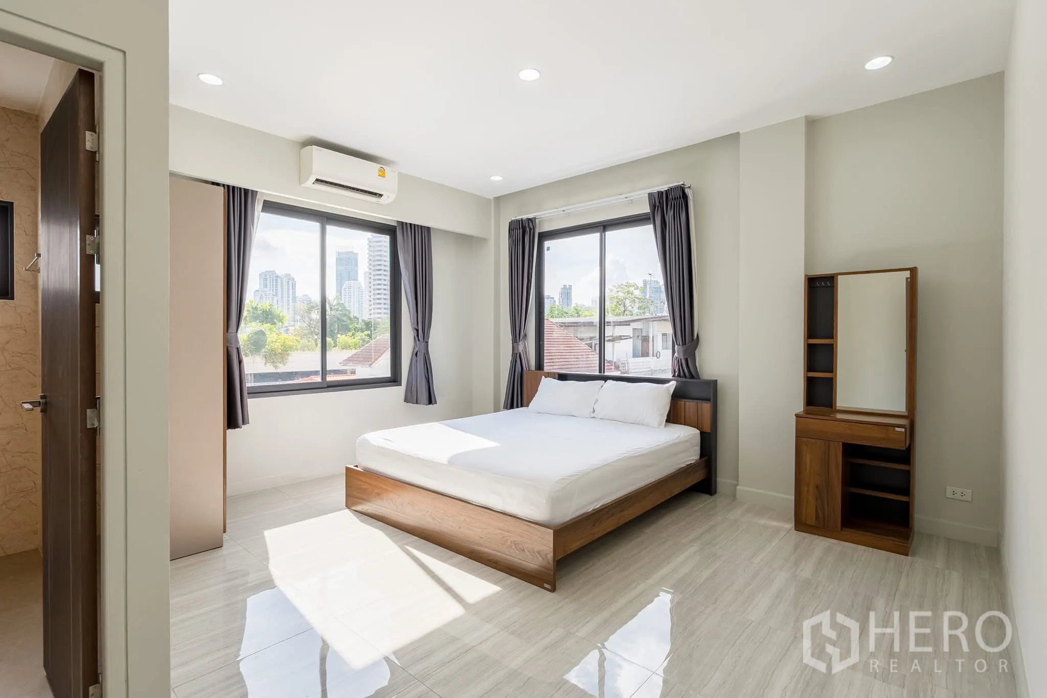 Home Office for rent in Khlong Toei, Bangkok - Sunlit bedroom with double bed, large windows, air conditioning and city skyline view.