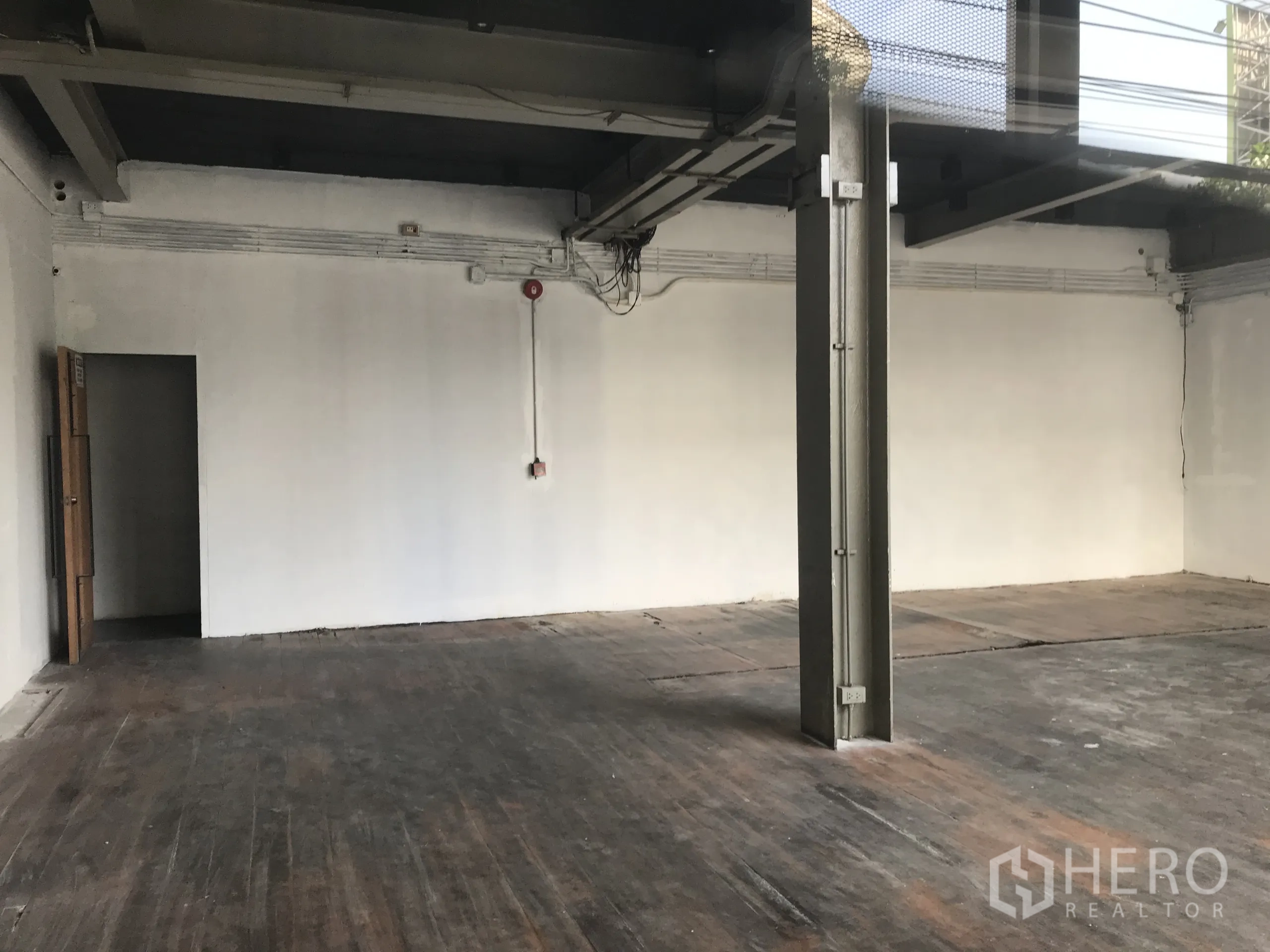 Retail Space for rent in Watthana, Bangkok - Open retail hall with a steel column, surface-mounted conduits on white walls, and wide plank flooring.